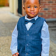 Sekou participe au concours pour gagner de l'argent avec cette photo : child, boy, smile, formal_wear, vest, bow_tie, white_shirt, portrait, standing, outdoor, confident, short_hair, fashion, cute, person, young, happy, background_blur, brick_wall, hands