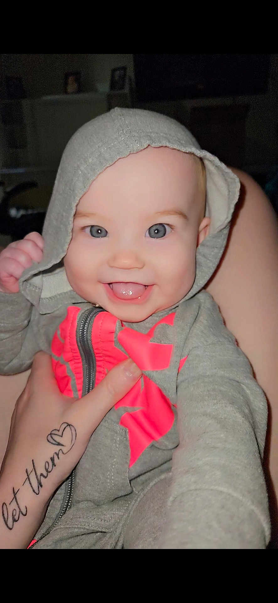 Aviana is registered to the contest to win money with this photo: baby, hoodie, smiling, tongue, hand, tattoo, indoor, clothing, person, face, child, cute, happy, gray, pink, zipper, skin, portrait, young, warm