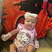 Gracelyn is registered to the contest to win money with this photo: baby, smiling, hello_kitty, pink_clothing, mittens, socks, headband, bow, chair, blanket, bicycle_design, indoors, cute, child, infant, happy, portrait, seated, soft_lighting, colorful