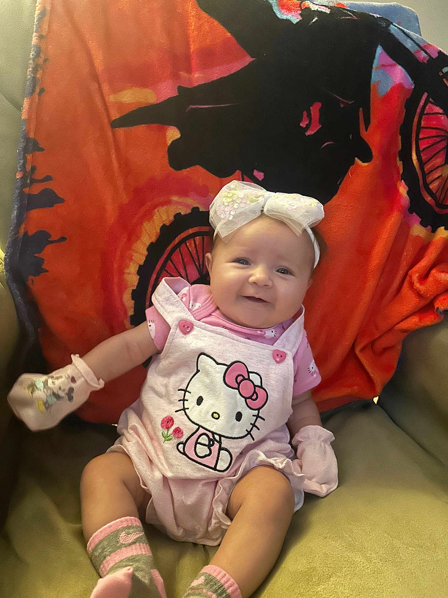 Gracelyn is registered to the contest to win money with this photo: baby, smiling, hello_kitty, pink_clothing, mittens, socks, headband, bow, chair, blanket, bicycle_design, indoors, cute, child, infant, happy, portrait, seated, soft_lighting, colorful