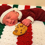 Asher is registered to the contest to win money with this photo: newborn, baby, sleeping, cookie, knit_hat, knit_suit, blanket, crochet, red, green, white, chocolate_chip_cookie, hand, face, infant, cute, resting, indoors, holiday, cozy