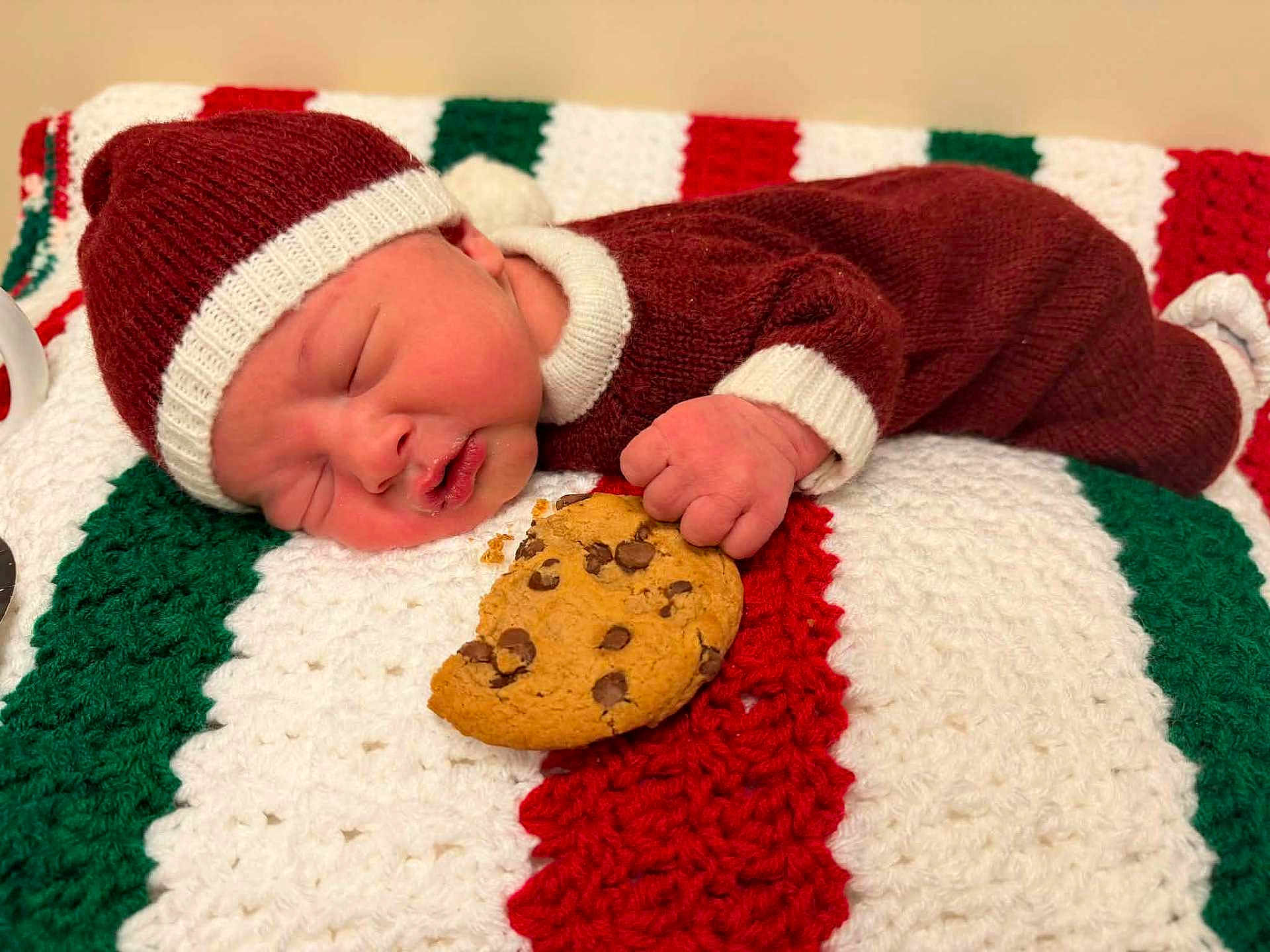 Asher is registered to the contest to win money with this photo: newborn, baby, sleeping, cookie, knit_hat, knit_suit, blanket, crochet, red, green, white, chocolate_chip_cookie, hand, face, infant, cute, resting, indoors, holiday, cozy