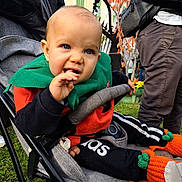 Mathys participe au concours pour gagner de l'argent avec cette photo : baby, stroller, child, outdoor, autumn, grass, people, clothing, pumpkin_booties, green_scarf, black_pants, orange_sweater, hand, face, blue_eyes, nibbling, person, jacket, background, fall_leaves