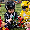 child, costume, helmet, toy, grass, outdoor, play, action_figure, red, black, yellow, pink, superhero, team, fun, kid, game, park, sitting, children