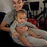 woman, baby, indoor, striped_clothing, smile, exercise_bike, blanket, holding, seated, person, happy, casual_clothing, home, adult, child, family, comfort, toddler, living_room, relaxed