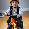 Nathaniel is registered to the contest to win money with this photo: toddler, child, helmet, balance_bike, orange, indoor, flooring, jacket, socks, toy, person, young_child, expression, riding, wood_floor, sporty, play, cute, concentration, helmet_design