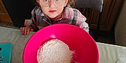 Ambre participe au concours pour gagner de l'argent avec cette photo : child, curly_hair, glasses, pink_bowl, flour, kitchen, wooden_cabinets, table, sugar_packet, yellow_bowl, curious, indoors, person, baking, food_preparation, cooking, young_child, home, appliance, chair