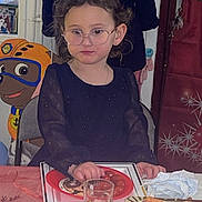 Ambre participe au concours pour gagner de l'argent avec cette photo : child, glasses, curly_hair, sitting, table, food, snacks, drinks, plate, glass, indoor, party, coat, cartoon_character, paw_patrol, curtains, window, napkins, person, celebration