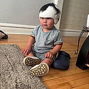 Eliot joined the competition — help win amazing prizes! baby, casual_clothing, child, cozy, curious, floor, footwear, grey_shirt, headgear, helmet, home, indoor, person, rug, shoes, shorts, sitting, toddler, wooden_floor, young_child