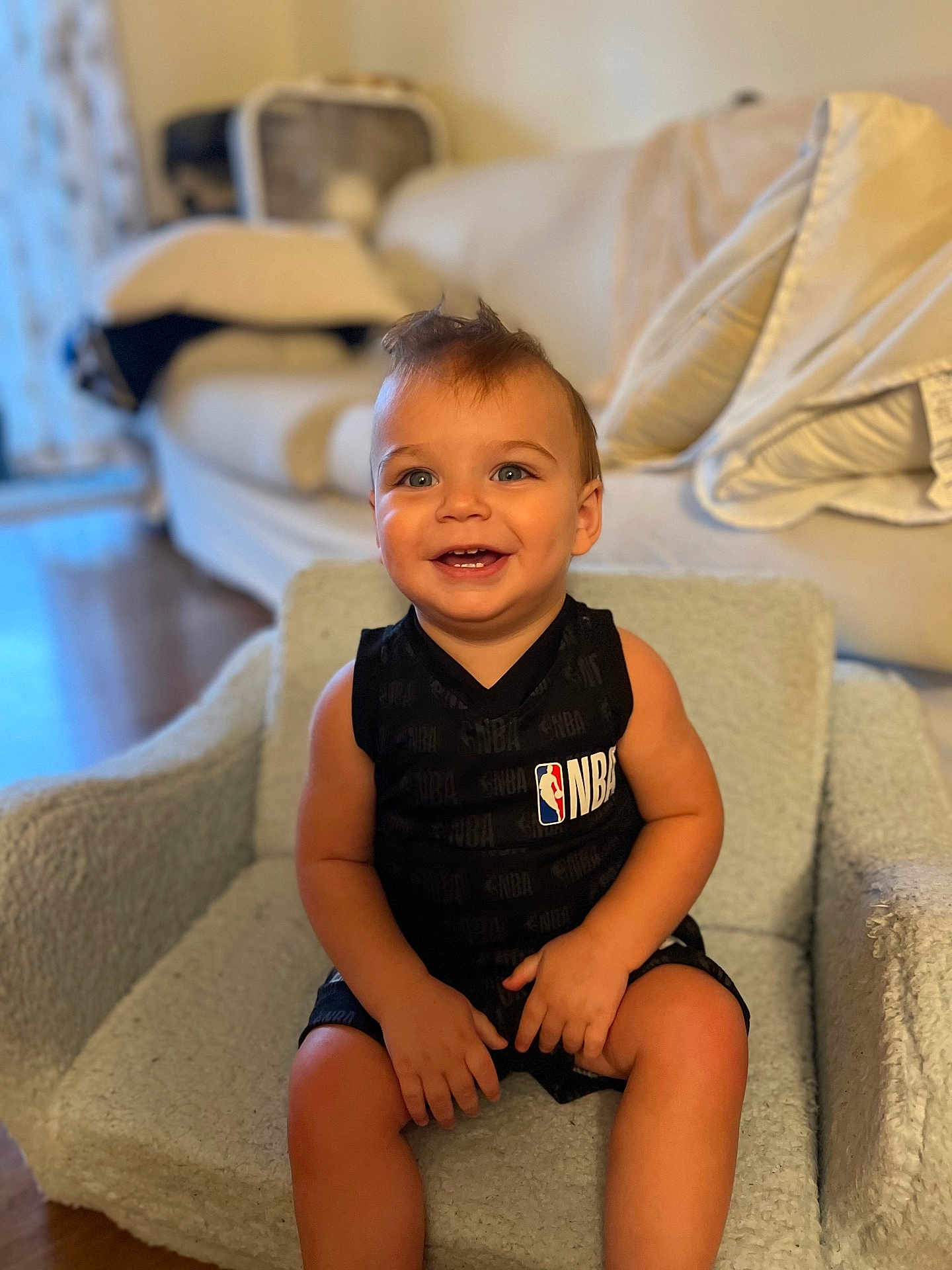 Michael is registered to the contest to win money with this photo: toddler, child, smiling, sitting, nba_jersey, black_clothing, moawk_hair, indoor, chair, couch, fan, happy, cute, person, portrait, home, furniture, wooden_floor, baby, small_hands
