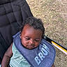 baby, infant, child, stroller, bib, sleepy, portrait, outdoor, grass, seated, harness, straps, curly_hair, facial_expression, clothing, green_outfit, blue_bib, photography, closeup, park