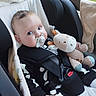 baby, child, car_seat, pacifier, plush_toy, stuffed_animal, cow_toy, black_clothing, seatbelt, window, car_interior, blanket, infant, hand, face, blue_eyes, cute, portrait, sitting, indoors