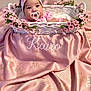 Kairo is registered to the contest to win money with this photo: baby, infant, pink, pacifier, headband, bow, wicker_basket, flowers, blanket, silk, embroidered_name, cute, portrait, indoors, soft_lighting, child, newborn, smiling, decorative, cozy