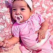 Kairo joined the competition — help win amazing prizes! baby, pacifier, pink_clothing, headband, bow, infant, blanket, floral_pattern, cute, child, portrait, lying_down, soft_texture, indoors, adorable, skin, hand, face, eyes, sleepwear