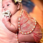 Kairo is registered to the contest to win money with this photo: baby, infant, pacifier, flower_headband, pearl_necklace, peach_fabric, blanket, newborn, cute, sleepy, soft_lighting, portrait, closeup, skin, hand, foot, lying_down, indoors, warm_colors, adorable