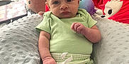 Caspian is registered to the contest to win money with this photo: baby, child, infant, plush_toy, pillow, green_clothing, soft_texture, indoor, seated, cute, face, hand, foot, expression, toy, blanket, person, room, stuffed_animal, casual