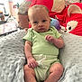 baby, child, infant, plush_toy, pillow, green_clothing, soft_texture, indoor, seated, cute, face, hand, foot, expression, toy, blanket, person, room, stuffed_animal, casual