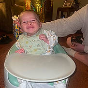Caspian joined the competition — help win amazing prizes! baby, bumbo_chair, smiling, infant, onesie, bib, happy, indoor, carpet, adult_hand, gift_bag, table, flower_pot, framed_photo, footwear, person, supporting_hand, cozy, living_room, cute