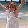arms_raised, beach, child, fun, happy, joy, ocean, outdoor, pier, playful, portrait, sand, smiling, summer, sunlight, sunny, toddler, waves, white_dress, windy