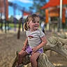 child, toddler, playground, outdoor, smiling, sitting, tree_branch, sneakers, purple_shorts, light_shirt, pigtails, sunny, play_equipment, sand, happy, person, daylight, casual_clothing, park, fun