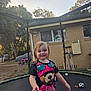 Diamond is registered to the contest to win money with this photo: child, toddler, smile, trampoline, tshirt, bear_graphic, outdoor, yard, fence, house, tree, toy, soccer_ball, purple_mat, grass, sunset, person, happy, play, daylight