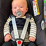 baby, pacifier, car_seat, child, infant, straps, seatbelt, black_clothing, striped_shirt, safety, comfort, indoors, cute, smiling, young_child, face, hands, head, car_safety, happiness