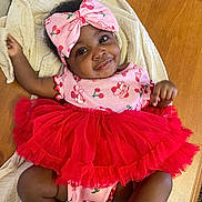 Fawlyn is registered to the contest to win money with this photo: baby, blanket, cherry, child, clothing, cute, fashion, happy, headband, indoors, infant, lying_down, person, pink, portrait, red, smile, toddler, tutu, wooden_table