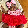 baby, child, smile, tutu, headband, pink, red, cherry, blanket, wooden_table, cute, infant, happy, portrait, clothing, lying_down, indoors, person, toddler, fashion