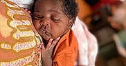 Fawlyn is registered to the contest to win money with this photo: baby, blanket, blurred_background, child, closeup, comfort, cozy, cuddle, curly_hair, face, hand, indoor, infant, orange_shirt, peaceful, pillow, portrait, rest, sleeping, soft_texture