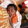 Fawlyn is registered to the contest to win money with this photo: baby, sleeping, orange_shirt, pillow, blanket, indoor, cozy, child, peaceful, curly_hair, face, hand, soft_texture, blurred_background, rest, portrait, infant, cuddle, comfort, closeup