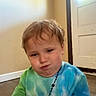 Kingston is registered to the contest to win money with this photo: beaded_necklace, casual_clothing, child, cute, door, expression, face, floor, hair, indoor, natural_light, person, portrait, pout, seated, skin, tie_dye_shirt, toddler, wall, young_child