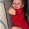 toddler, child, smiling, red_shirt, diaper, indoor, narrow_space, shoe, leopard_print, curly_hair, playful, happy, wall, carpet, furniture, cute, face, portrait, baby, candid
