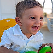 Joseph is registered to the contest to win money with this photo: toddler, child, smile, happy, toy, green, yellow, chair, white_shirt, short_hair, portrait, indoors, hands, face, cute, playful, bright, daylight, closeup, person