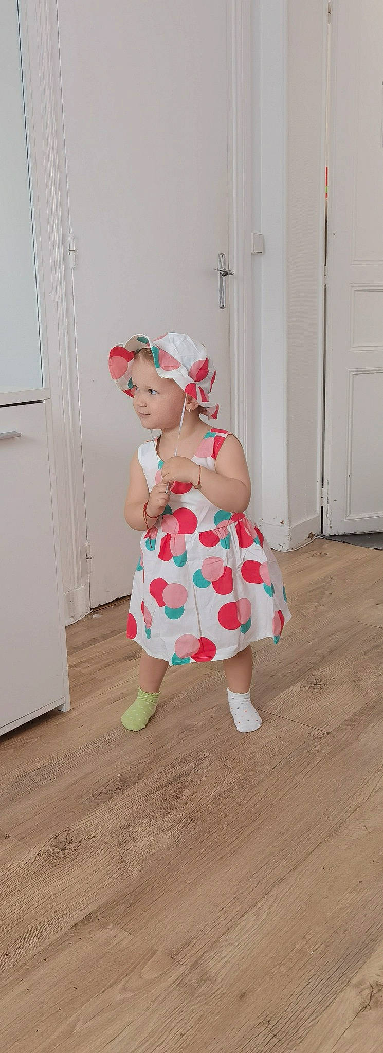 Alexandra participe au concours pour gagner de l'argent avec cette photo : baby, baby_toddler_clothing, baseball_cap, cap, day_dress, door, dress, floor, flooring, happy, hardwood, headwear, human_leg, knee, one_piece_garment, pattern, person, sleeve, thigh, toddler