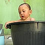 adult_face, baby, bath_time, candid, child, container, curious_expression, floor, green_wall, home_setting, inset_thumbnail, outdoor, peeling_paint, plastic_tub, portrait, potted_plants, shelf, tiles, video_call, wet_hair