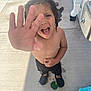 child, boy, hand, face, curly_hair, open_mouth, outdoor, concrete, water, wet_skin, black_shorts, black_shoes, green_cup, playful, summer, sunlight, drinking_fountain, towel, slippers, background_objects