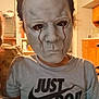 child, mask, face, costume, indoor, shirt, text, person, portrait, hair, sitting, lighting, kitchen, furniture, casual, expressionless, spooky, halloween, home, candid