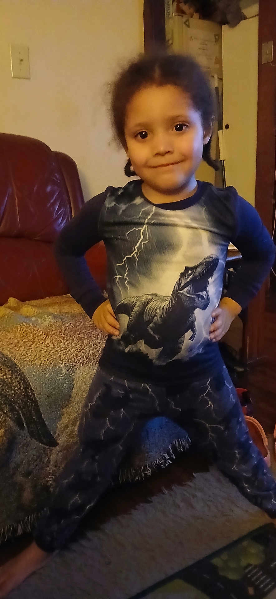 Jewlz joined the competition — help win amazing prizes! child, dinosaur, tshirt, pants, lightning, indoor, living_room, carpet, blanket, furniture, person, smile, standing, hair, face, expression, clothing, cozy, leather_chair, home