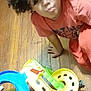 Jewlz is registered to the contest to win money with this photo: child, curly_hair, red_shirt, red_pants, wooden_floor, toy, plastic_toy, toy_track, small_vehicle, indoor, playtime, kneeling, young_child, casual_clothing, flooring, expression, looking_down, hand, toy_car, colorful