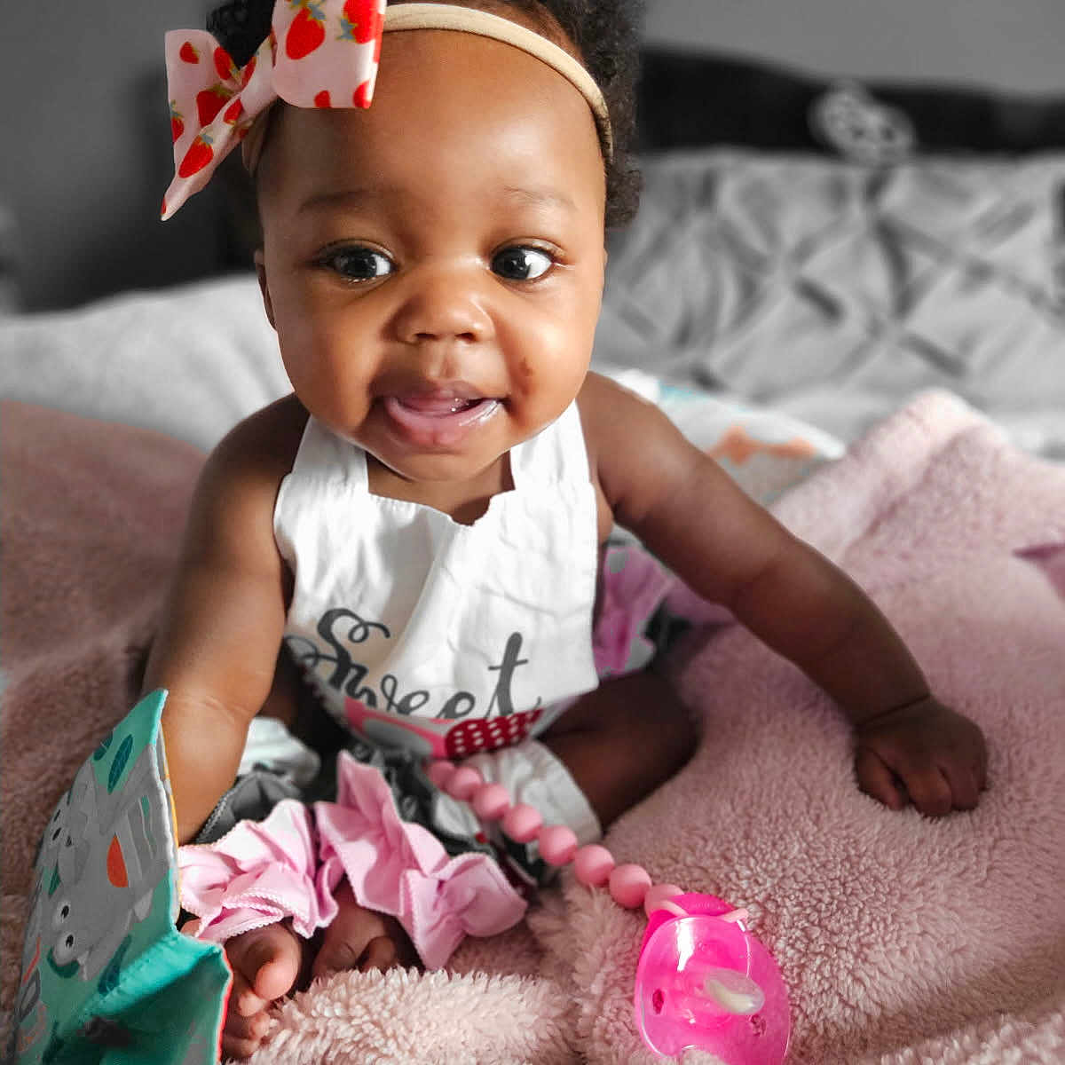 Algeria joined the competition — help win amazing prizes! baby, child, infant, cute, smiling, curly_hair, headband, bow, toy, blanket, pink, white_clothing, indoors, soft_texture, focus, portrait, happy, sitting, face, playful