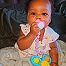 Algeria is registered to the contest to win money with this photo: baby, child, pacifier, toy, blanket, curly_hair, indoor, bed, cute, infant, sitting, clothing, pink, blue, orange, yellow, face, hand, portrait, young
