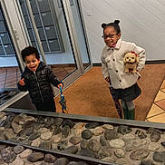 Joséphine joined the competition — help win amazing prizes! child, children, indoor, glass_door, umbrella, stuffed_animal, coat, jacket, glasses, smiling, playful, floor, rocks, decor, carpet, wall, person, happy, toy, boots