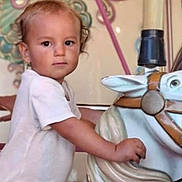 Thiago participe au concours pour gagner de l'argent avec cette photo : amusement_park, carousel, child, colorful, curly_hair, decorative, expression, face, hand, horse, indoor, person, play, portrait, ride, seat, toddler, toy, vintage, white_clothing