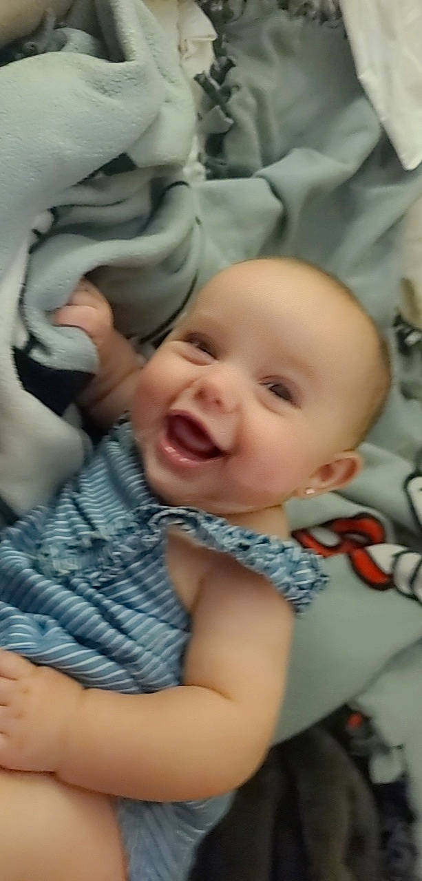 Nyomi is registered to the contest to win money with this photo: baby, baby_toddler_clothing, cheek, child, chin, comfort, eye, eyebrow, gesture, happy, iris, linens, mouth, nose, pattern, person, product, skin, smile, textile