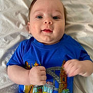 Milo participe au concours pour gagner de l'argent avec cette photo : baby, infant, child, blue_shirt, graphic_tshirt, lying_on_bed, blanket, portrait, face, eyes, smile, cheeks, hands, cute, closeup, skin, hair, bedroom, mouth, adorable