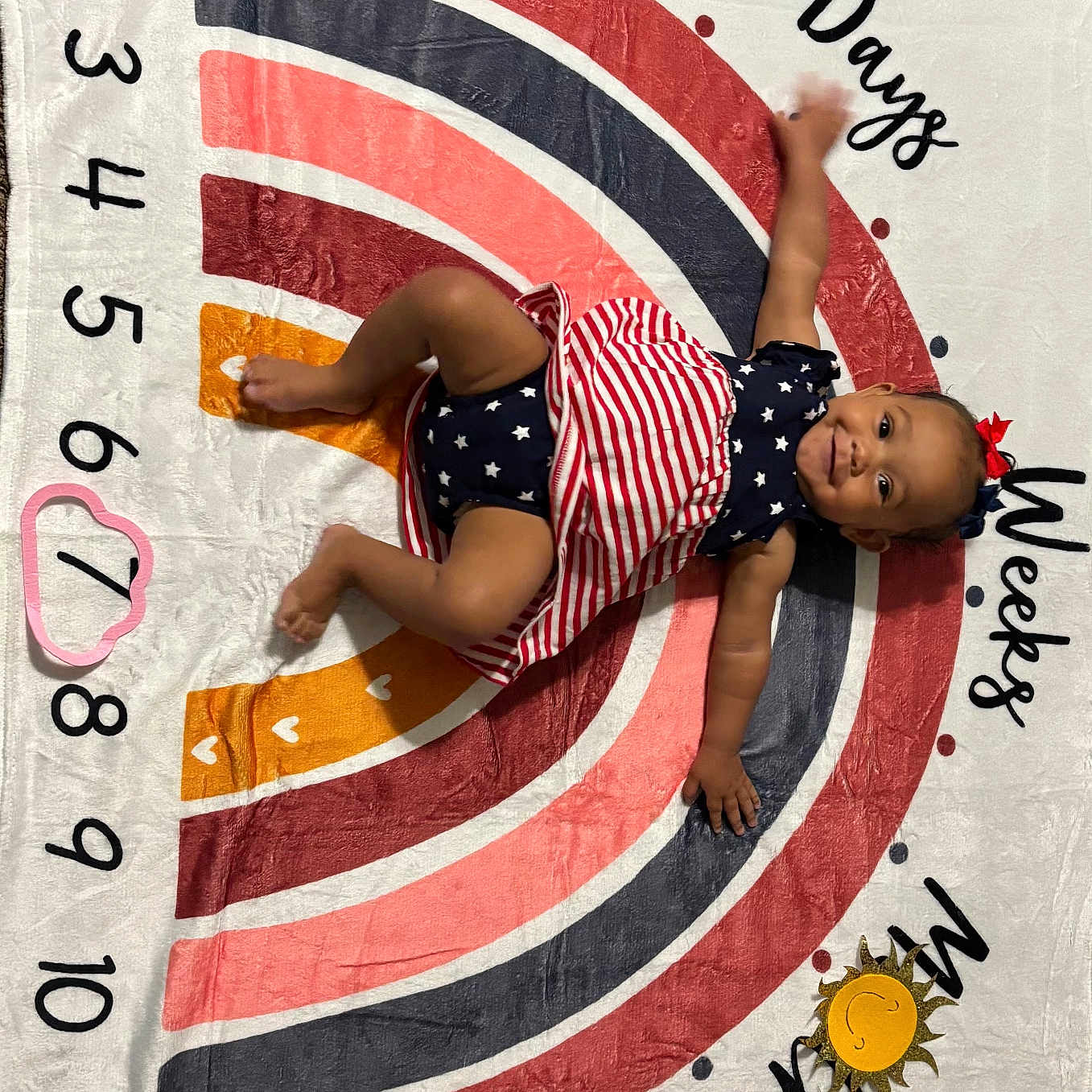Nova is registered to the contest to win money with this photo: baby, blue, clothing, colorful, dress, face, foot, hand, happy, infant, milestone_blanket, numbers, rainbow, red, smile, star_pattern, striped, sun_decoration, weeks, white