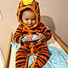 Lissandro participe au concours pour gagner de l'argent avec cette photo : adorable, blanket, blue_brush, changing_table, child, cozy, footed_pyjamas, hairbrush, hood, indoor, long_eyelashes, looking_down, onesie, orange, pajamas, sitting, stripes, tiger_costume, toddler, wooden_frame
