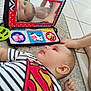 animal_illustration, baby, carpet, child, colorful, cute, floor, foot, hand, indoor, mirror, person, playtime, reflection, reflection_in_mirror, smiling, striped_clothing, superman_shirt, tile_floor, toy