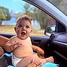 baby, child, diaper, car_interior, tattoo, hand, blue_towel, smiling, happy, person, skin, window, nature, outdoor, seat, adult, bracelet, expression, portrait, supporting_hand
