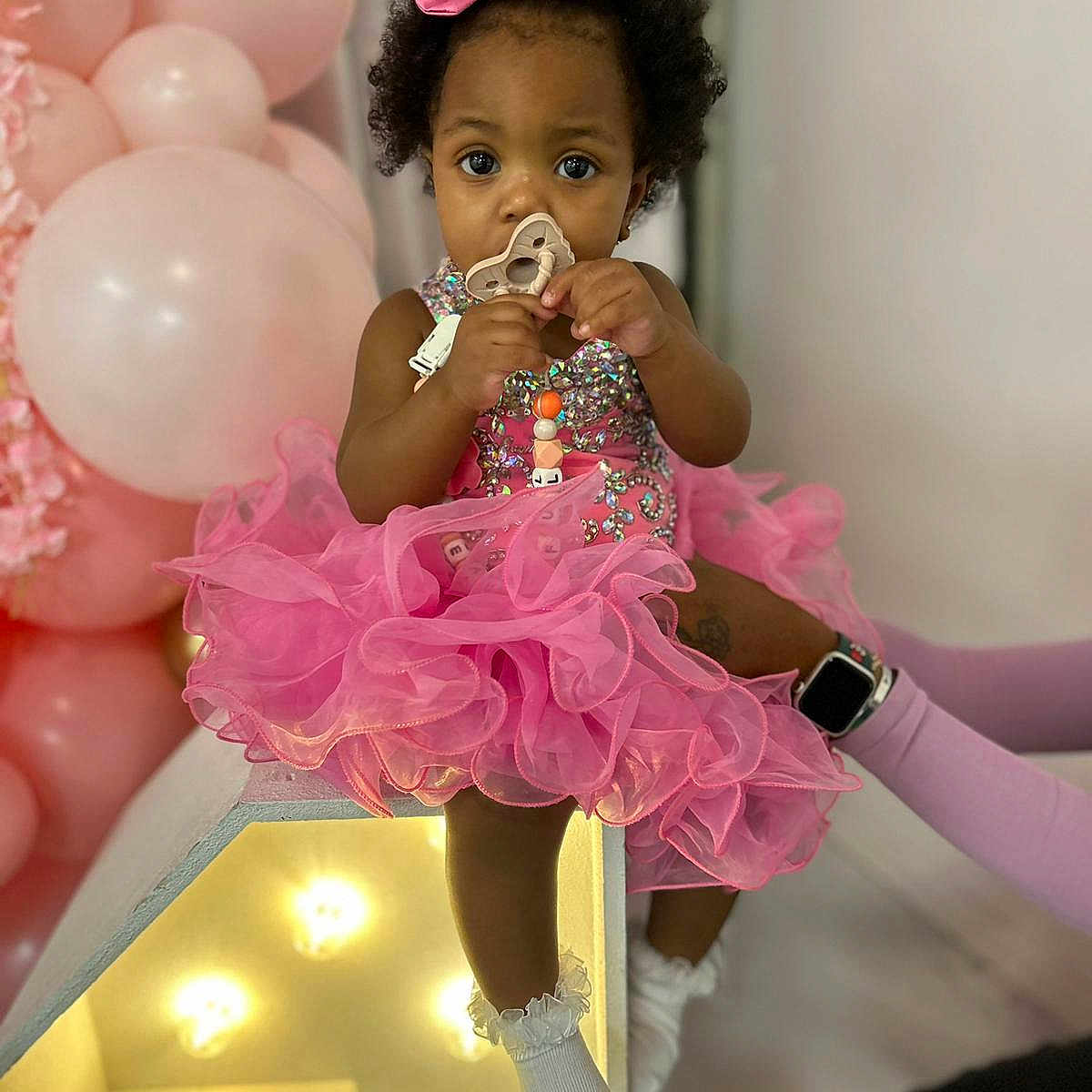 Beautiful is registered to the contest to win money with this photo: adorable, balloons, bow, celebration, child, curly_hair, cute, decorations, festive, indoor, light_box, pacifier, party, pink_dress, portrait, sitting, socks, sparkly, toddler, young_child